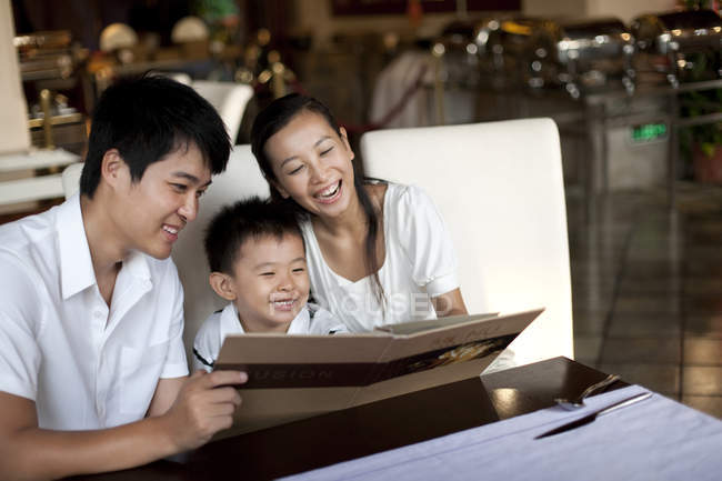 Chinese parents and son looking through menu in restaurant — Stock Photo
