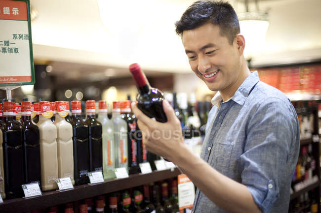 Hombre chino eligiendo vino en el supermercado - foto de stock