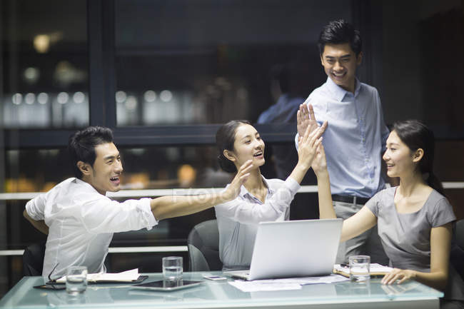 Chinese business team high fiving in meeting at evening — Stock Photo