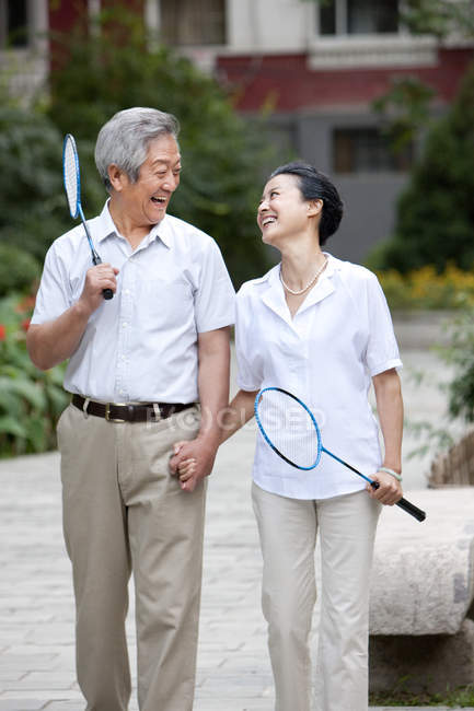 Senior pareja china caminando en el distrito residencial con raquetas de bádminton - foto de stock