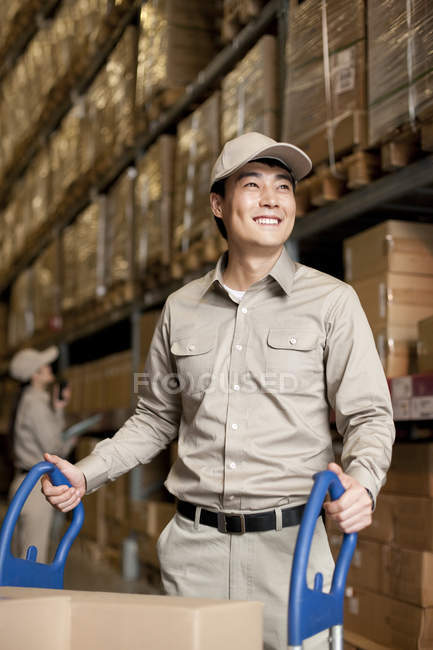 Homme chinois entrepôt travailleur poussant boîtes — Photo de stock