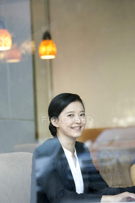 Empresaria china sentada en la cafetería y mirando en cámara - foto de stock
