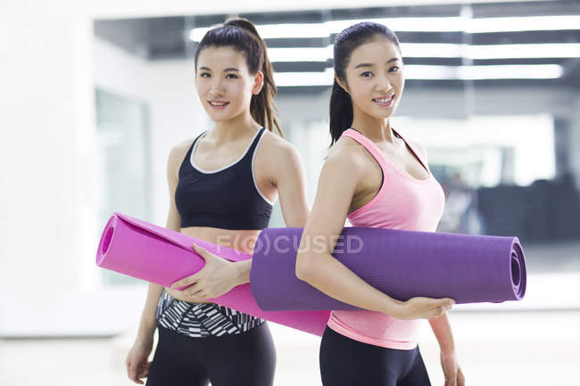Mujeres chinas sosteniendo colchonetas de yoga en el gimnasio - foto de stock