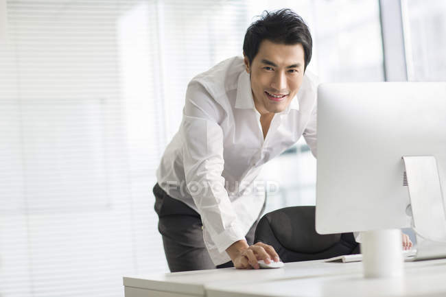 Hombre de negocios chino usando la computadora en la oficina y mirando en la cámara - foto de stock