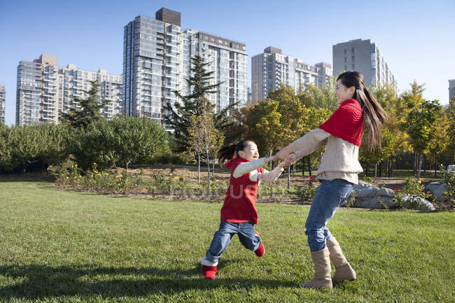 Chinese mother and daughter holding hands and spinning in park — Stock Photo