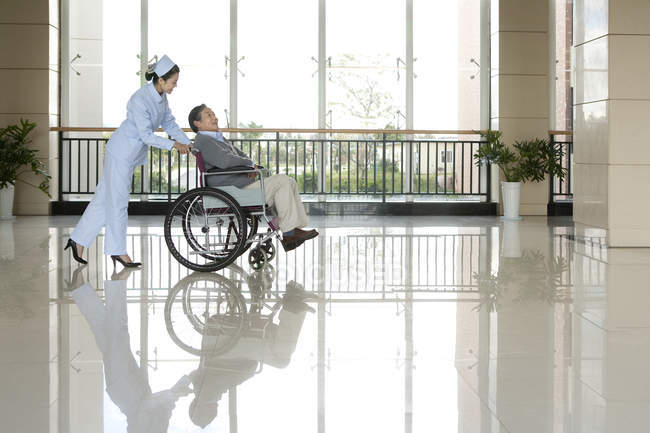 Enfermeira chinesa empurrando homem sênior em cadeira de rodas — Fotografia de Stock