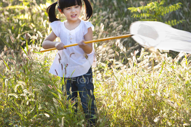 Little Chinese girl playing in meadow with butterfly net — Stock Photo