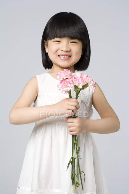 Little Chinese girl holding bunch of carnations on gray background — Stock Photo