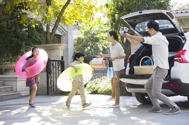 Chinese siblings wearing swimming tubes running to car with parents — Stock Photo