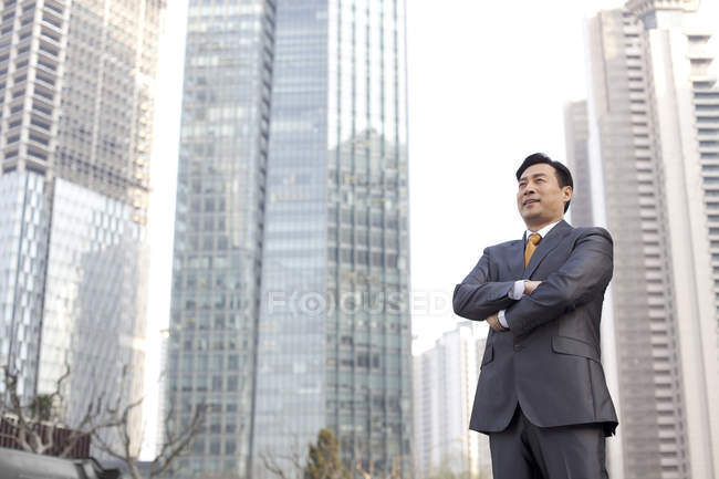 Chinese businessman standing with arms crossed in financial district — Stock Photo