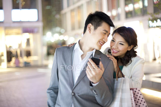 Couple chinois utilisant un smartphone tout en faisant du shopping en ville — Photo de stock