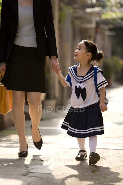 Chinese schoolgirl walking with mother on street — Stock Photo