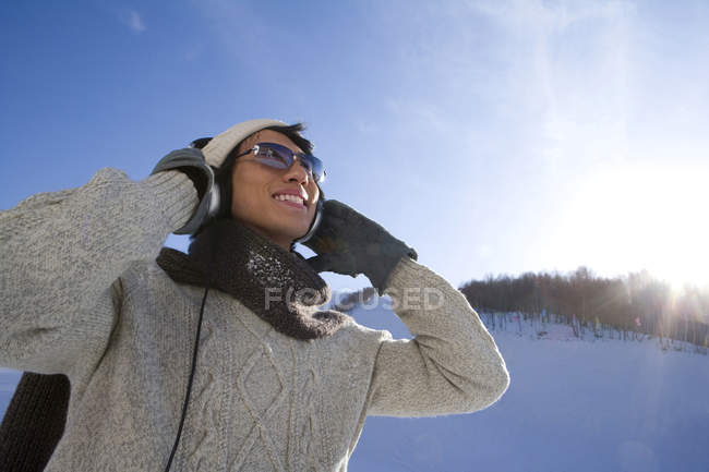 Hombre chino con auriculares sonriendo en la estación de esquí - foto de stock