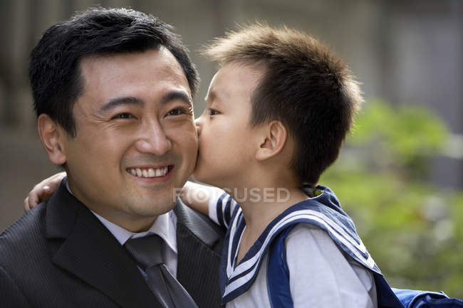 Chinese schoolboy kissing father on cheek — Stock Photo