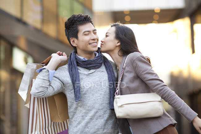 Веселая китаянка целует мужчину с сумками на улице — стоковое фото