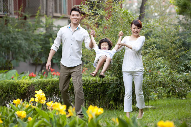 Chinese parents holding hands with swinging son in city garden — Stock Photo