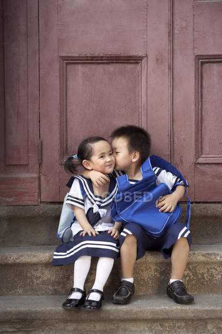 Chinese schoolboy kissing schoolgirl on porch — Stock Photo