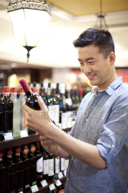 Hombre chino eligiendo vino en el supermercado - foto de stock