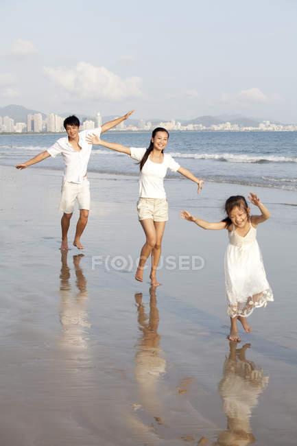 Китайская семья бежит по пляжу с протянутыми руками — стоковое фото