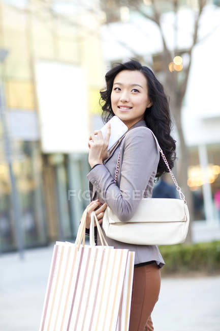 Chinese woman holding shopping bags and smartphone and looking at view on street — Stock Photo
