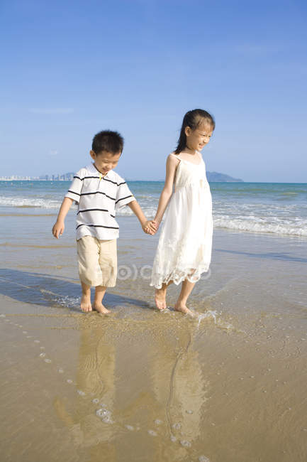 Chino elemental edad chica y chico caminando en playa - foto de stock