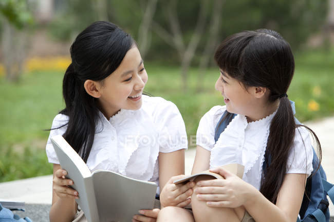 Schoolgirls sitting on steps, talking and reading books — Stock Photo