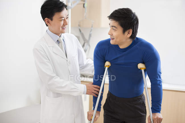 Médico chino ayudando al paciente con muletas - foto de stock
