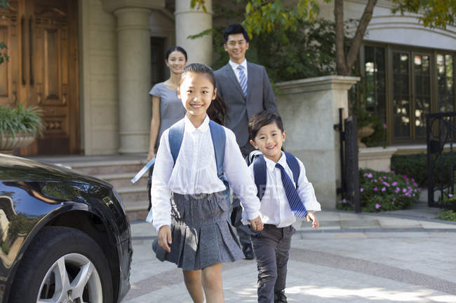 Chinese children holding hands and walking while parents watching in background — Stock Photo