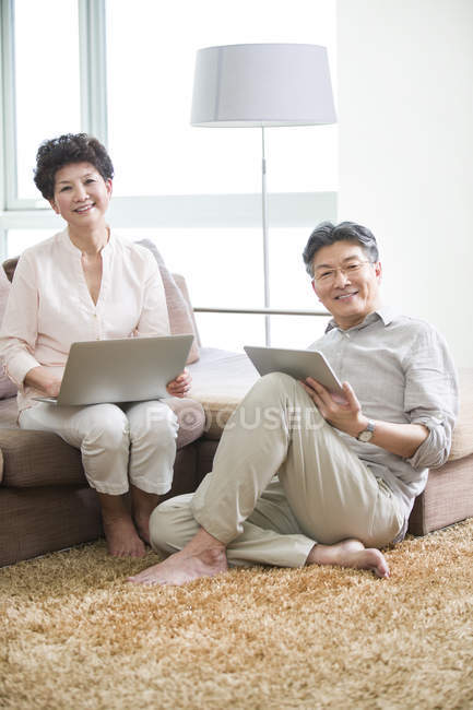 Chinese senior couple using laptop and digital tablet in living room — Stock Photo