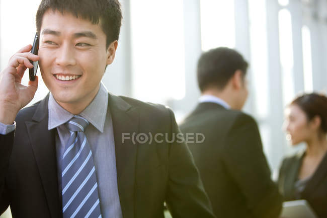 Китайский бизнесмен разговаривает по телефону с коллегами в фоновом режиме в помещении — стоковое фото