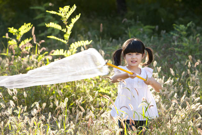 Kleines chinesisches Mädchen spielt auf Wiese mit Schmetterlingsnetz — Stockfoto