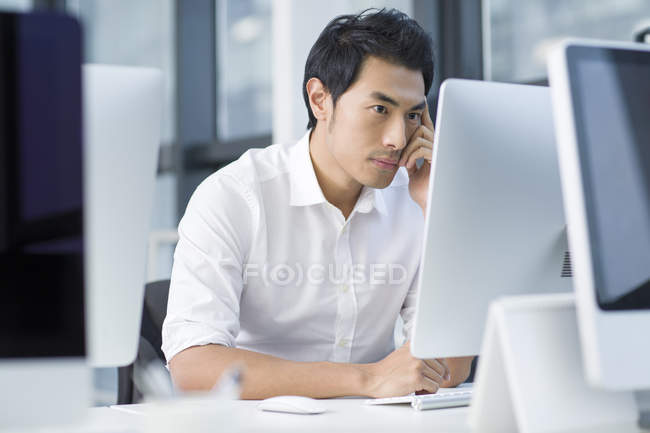 Китайский бизнесмен думает и пользуется компьютером в офисе — стоковое фото