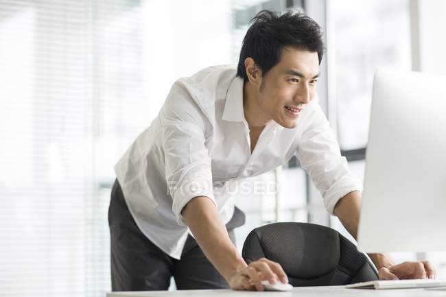 Homme d'affaires chinois debout et l'utilisation de l'ordinateur dans le bureau — Photo de stock