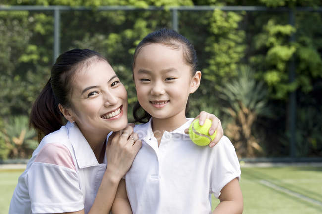 Chinese mother and daughter posing on tennis court — Stock Photo