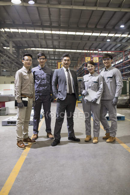 Maduro empresario chino y equipo de ingeniería posando en fábrica - foto de stock