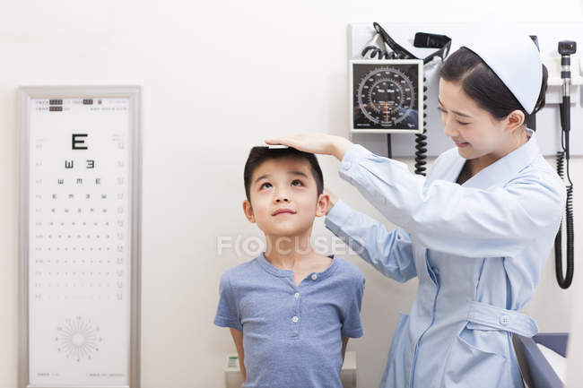 Китайская медсестра измеряет мальчика в смотровой — стоковое фото