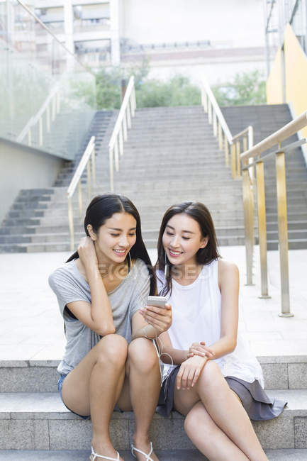 Chinese female friends listening to music on street stairs — Stock Photo