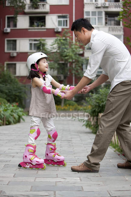 Chinese father helping daughter riding roller skates — Stock Photo
