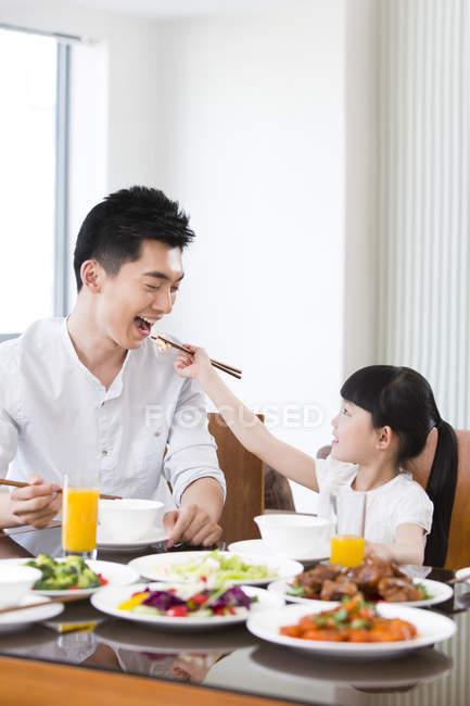 Chinese daughter feeding father with chopsticks while lunch — Stock Photo