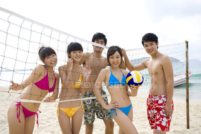 Китайские друзья позируют с сеткой для пляжного волейбола и мячом — стоковое фото