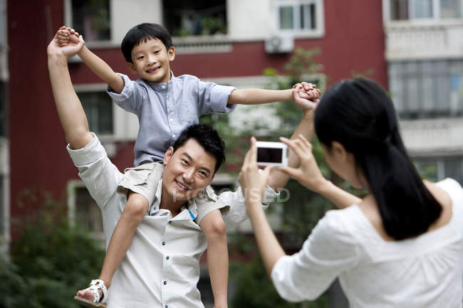 Madre tomando la foto del hombre llevando a su hijo en hombros - foto de stock