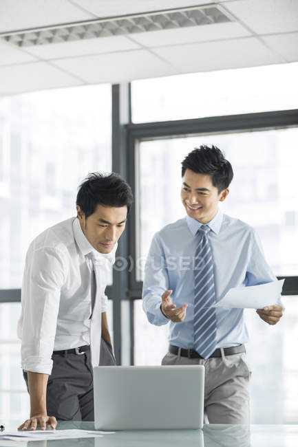 Китайские бизнесмены используют ноутбук и разговаривают в офисе — стоковое фото