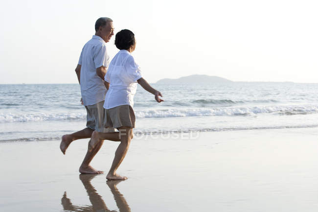 Senior Chinese couple running on beach sand — Stock Photo