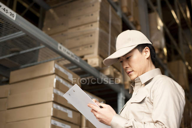 Male Chinese warehouse worker writing with clipboard — Stock Photo