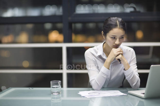 Empresaria china sentada con las manos cerradas en el escritorio en la oficina - foto de stock
