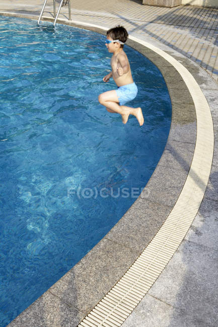 Petit garçon en lunettes de natation sautant dans l'eau de la piscine — Photo de stock