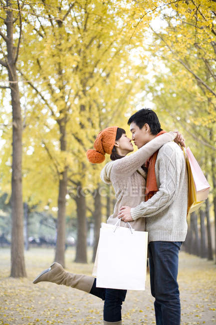 Chinese couple with shopping bags embracing and kissing in park — Stock Photo