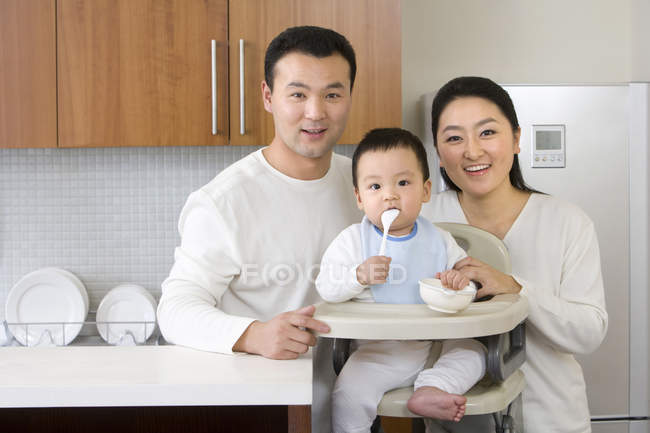 Famille chinoise avec bébé garçon en chaise haute dans la cuisine — Photo de stock