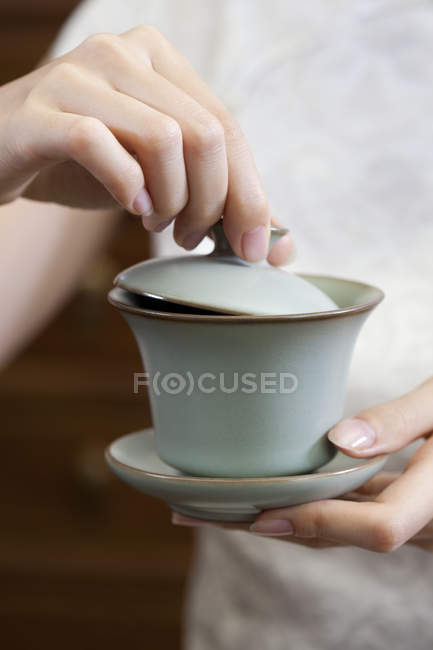 Primer plano de las manos femeninas sosteniendo la taza de té con tapa - foto de stock