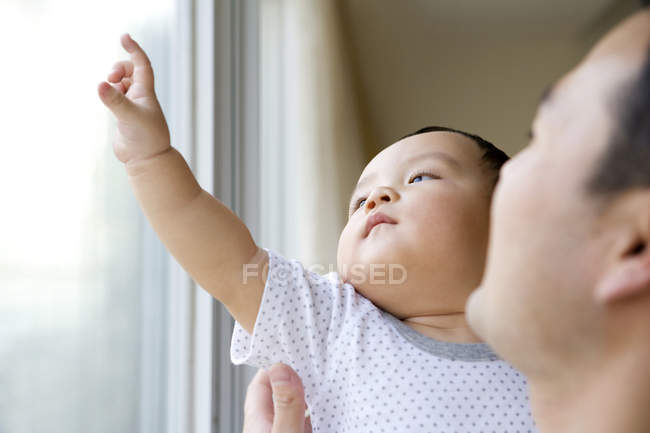 Hombre chino con niño mirando por la ventana y señalando - foto de stock